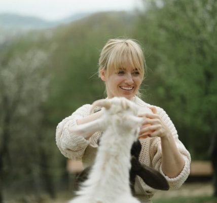 Joyful moment of a woman playing with a goat on a rural farm setting.