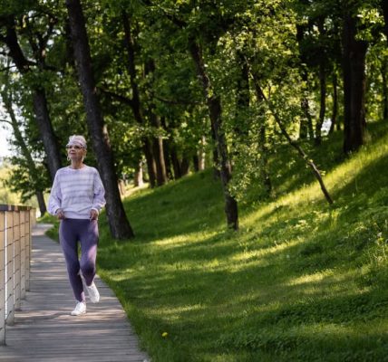 Elderly woman running along a riverside path in a green park, embracing fitness and nature.
